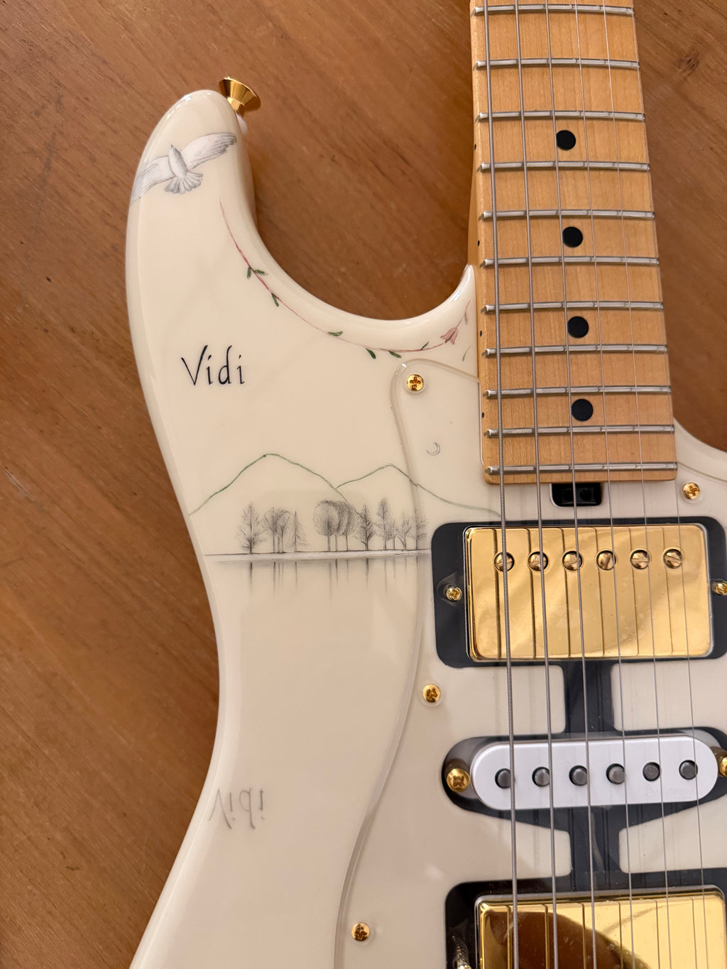 Close-up of a white electric guitar with pencil design on a wooden background