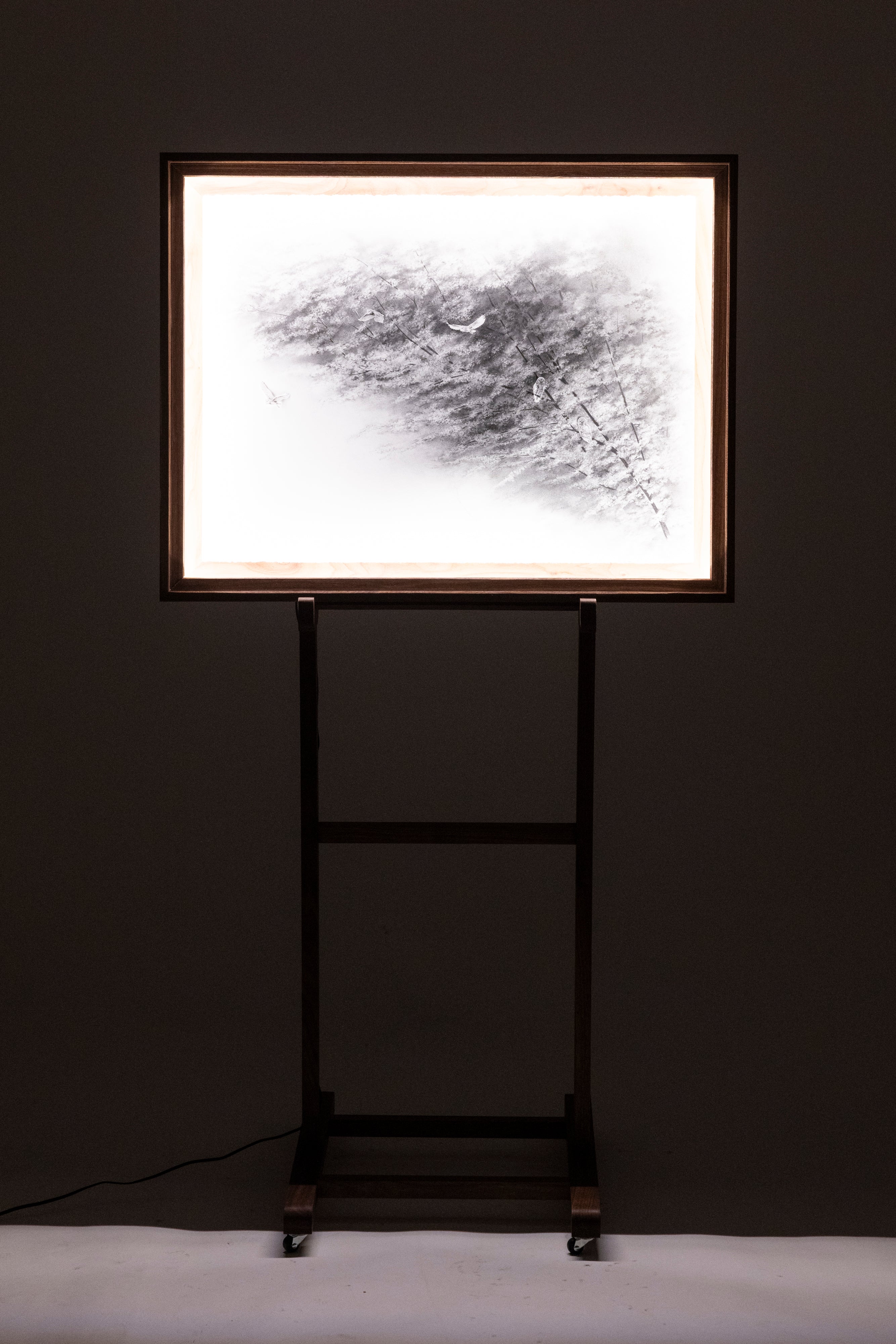 Framed abstract artwork on a stand against a dark wall
