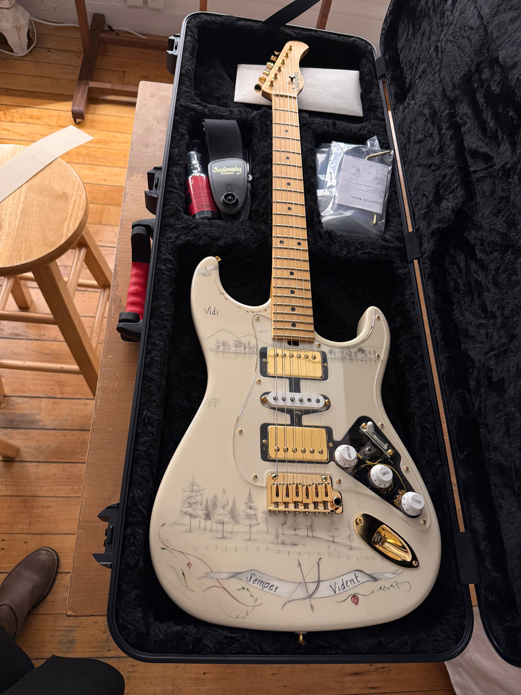 White electric guitar with gold hardware in a black case on a wooden floor.